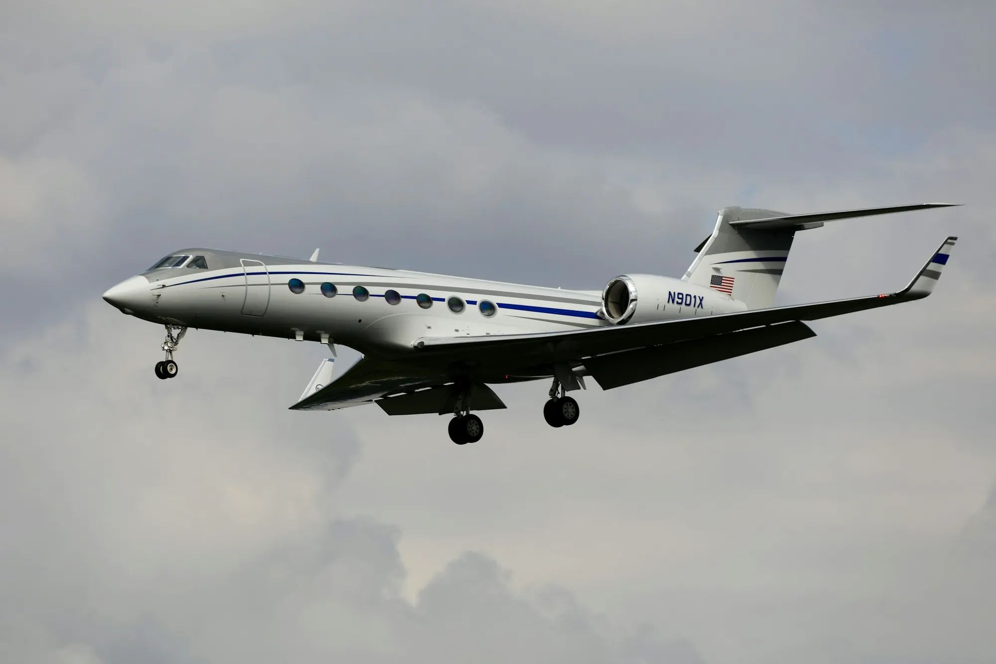 A large-cabin business jet in flight against a pale sky